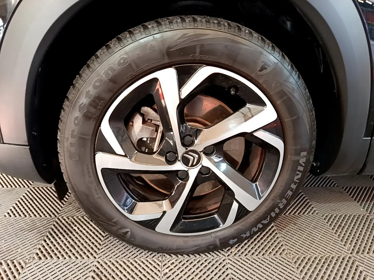 Gros plan sur la roue avant gauche noire du Citroën C5 Aircross Hybrid avec jante alliage bicolore et logo Citroën central.