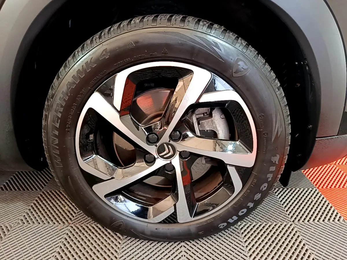 Gros plan sur la roue avant gauche du Citroën C5 Aircross Hybrid 225 ë-EAT8 Shine noir, jante alliage bicolore.
