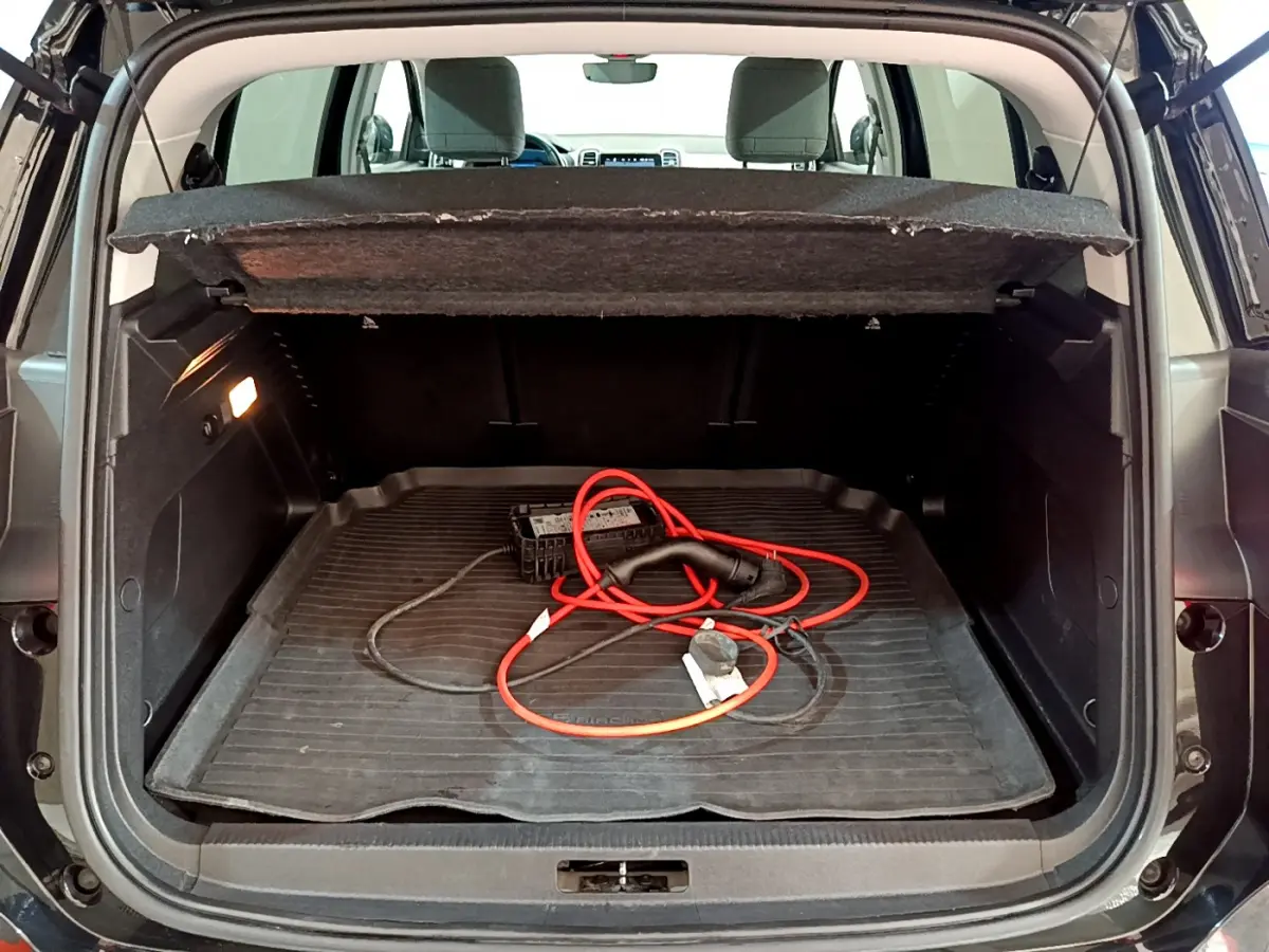 Coffre ouvert vu de l'arrière d'une Citroën C5 Aircross Hybrid noire avec câble de recharge rouge visible.