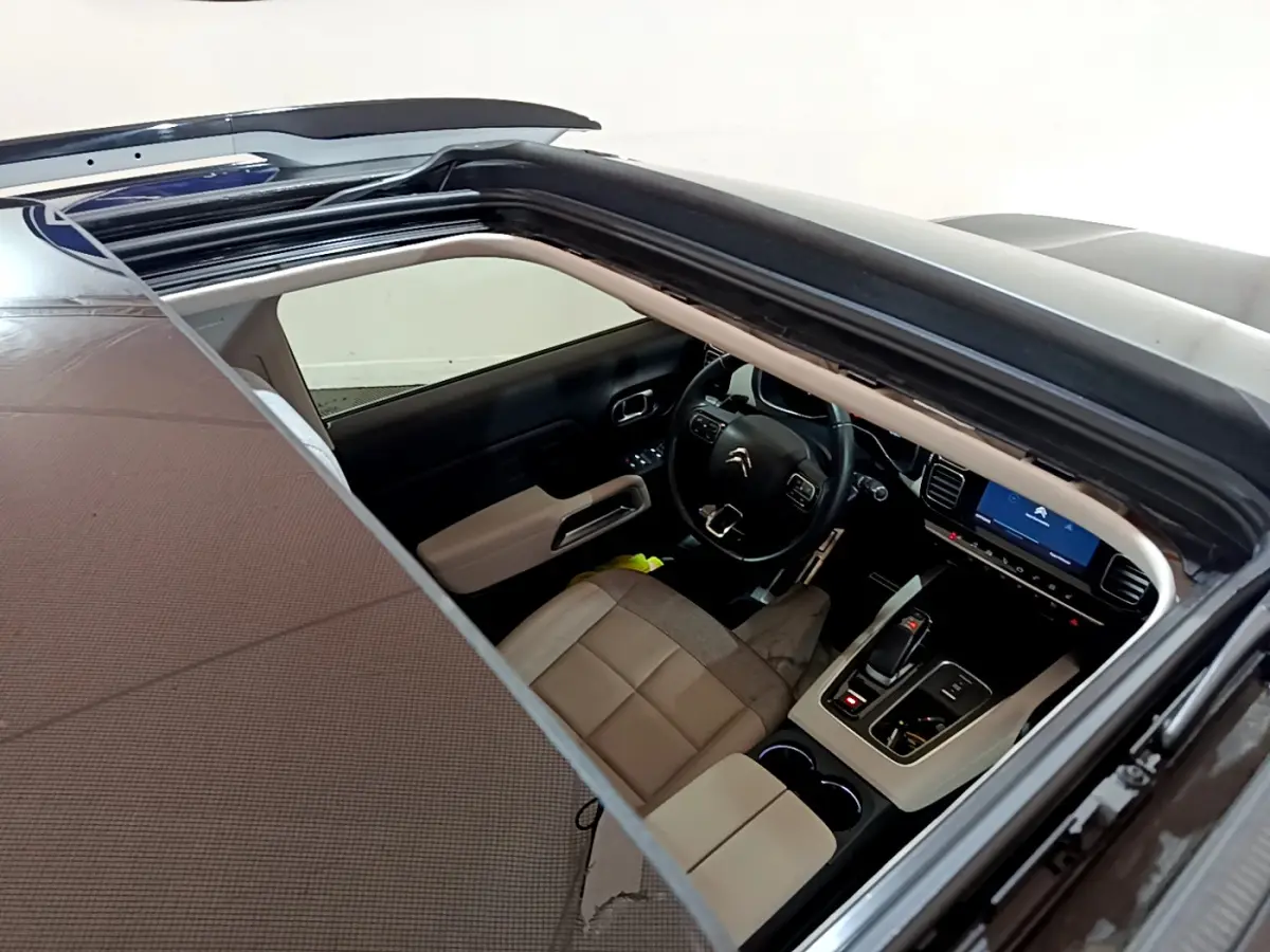 Vue intérieure par le toit ouvrant d'un Citroën C5 Aircross Hybrid noir, montrant le tableau de bord et sièges beige.