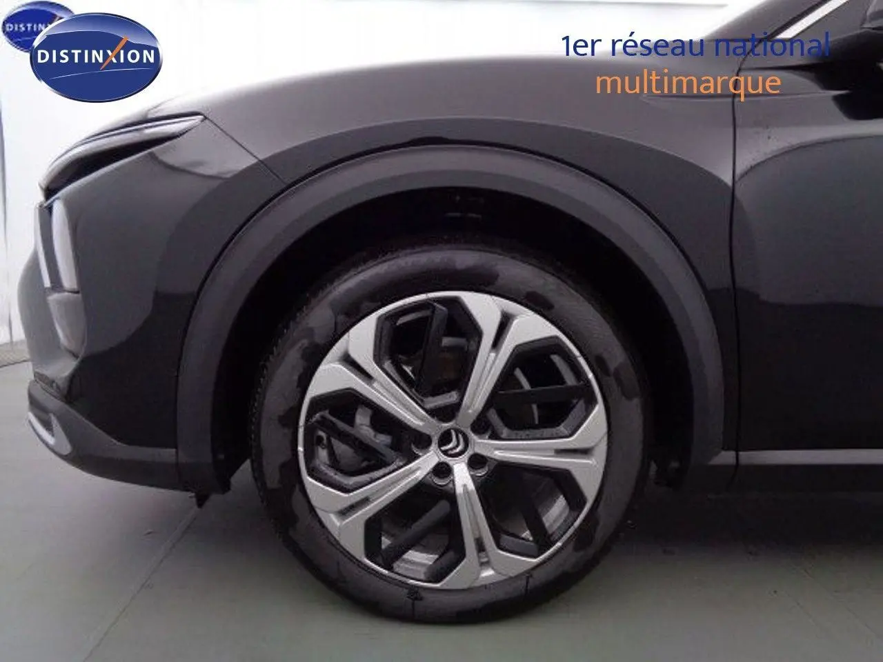 Gros plan sur la roue avant gauche du Citroën C5 X noir métal, mettant en valeur sa jante moderne à motifs géométriques.