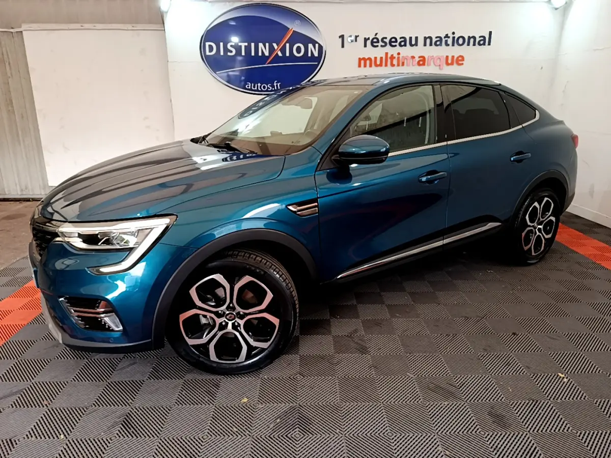 Renault Arkana Techno bleu en vue 3/4 avant droit, avec jantes distinctives et toit noir dans un showroom intérieur.