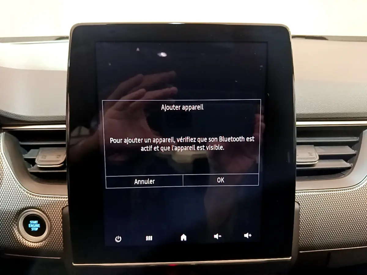 Écran tactile central allumé avec message Bluetooth, tableau de bord gris et bouton démarrage dans Renault Arkana bleu.