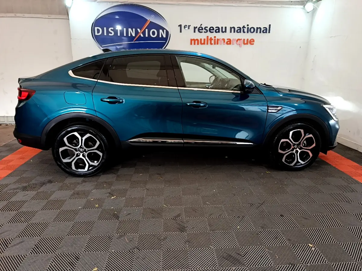 Profil droit d'une Renault Arkana Techno E-Tech bleu 2023 en hybride, avec jantes alliage distinctives et toit plongeant.