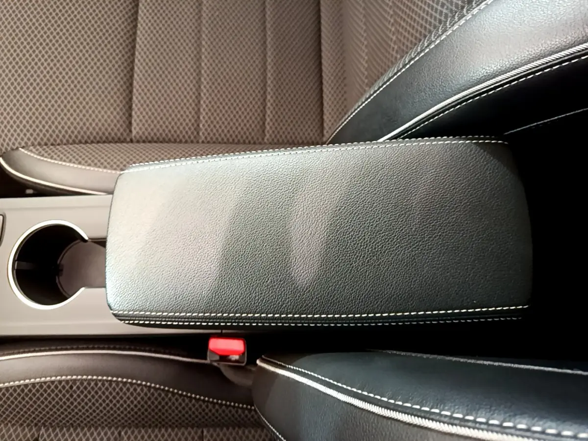 Détail de l'accoudoir central en cuir noir avec surpiqûres blanches et sièges tissu marron du Renault Arkana 2023.