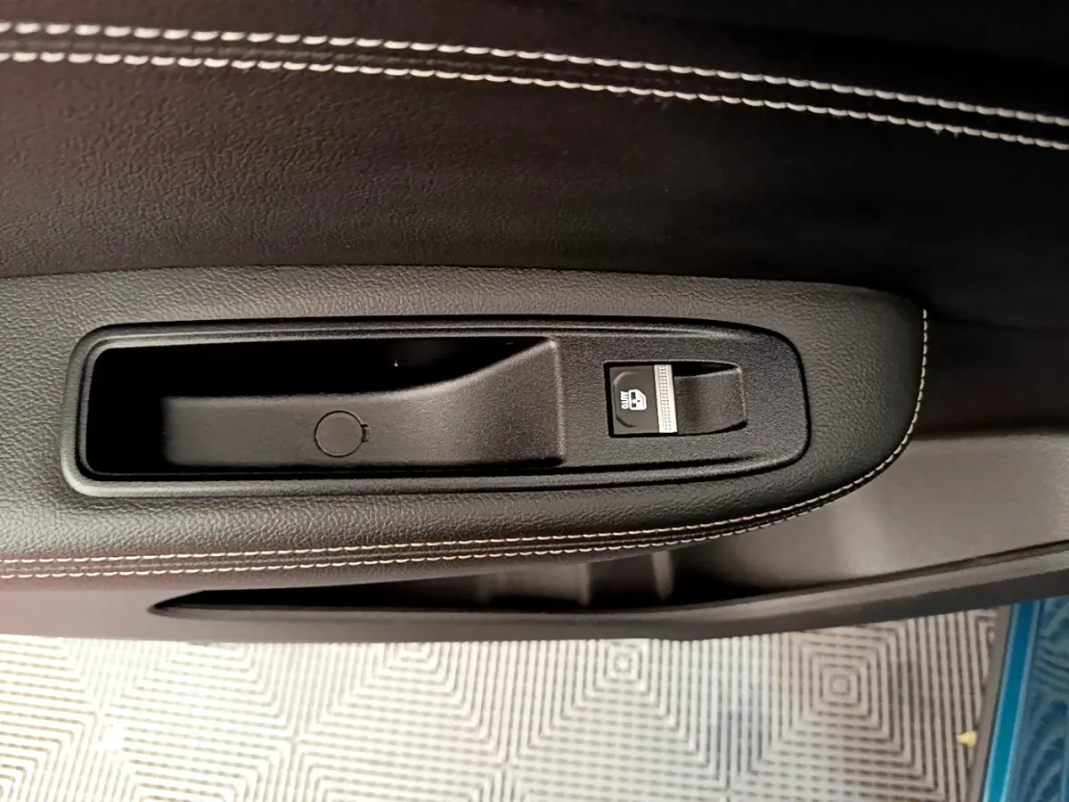 Gros plan sur la poignée intérieure noire avec bouton de verrouillage, sur la porte côté conducteur du Renault Arkana bleu.