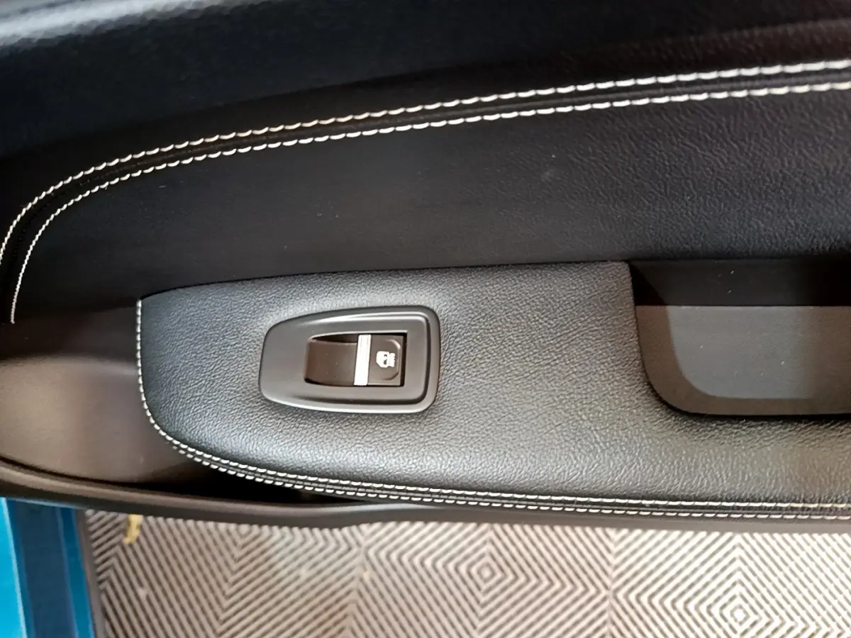 Gros plan sur la commande de verrouillage de porte noire avec surpiqûres blanches, intérieur d’une Renault Arkana bleu.