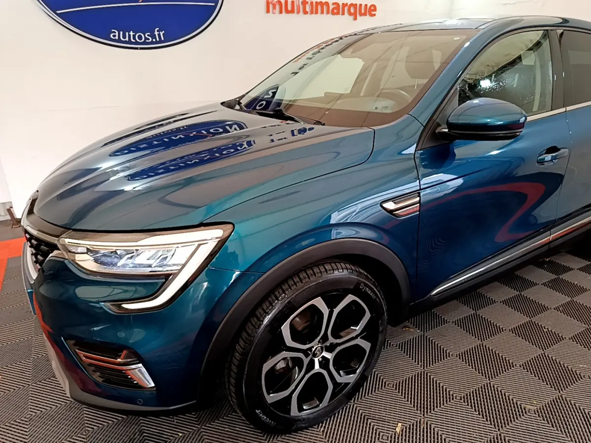 Vue 3/4 avant droit d'une Renault Arkana Techno E-Tech hybride bleu avec jantes noires et phares LED distinctifs.
