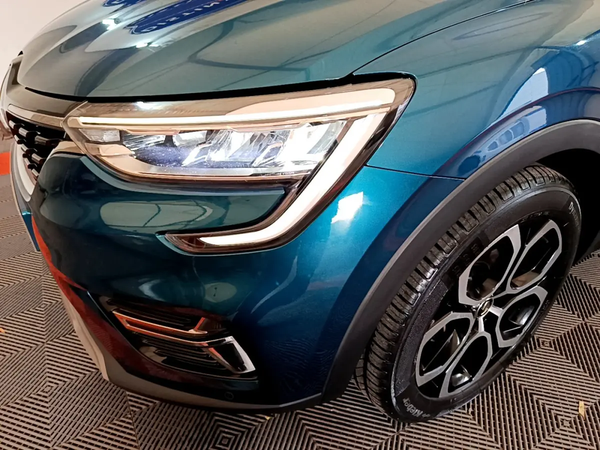 Gros plan sur l'avant droit bleu métallisé du Renault Arkana 2023, mettant en valeur le phare LED et la jante alu noire.