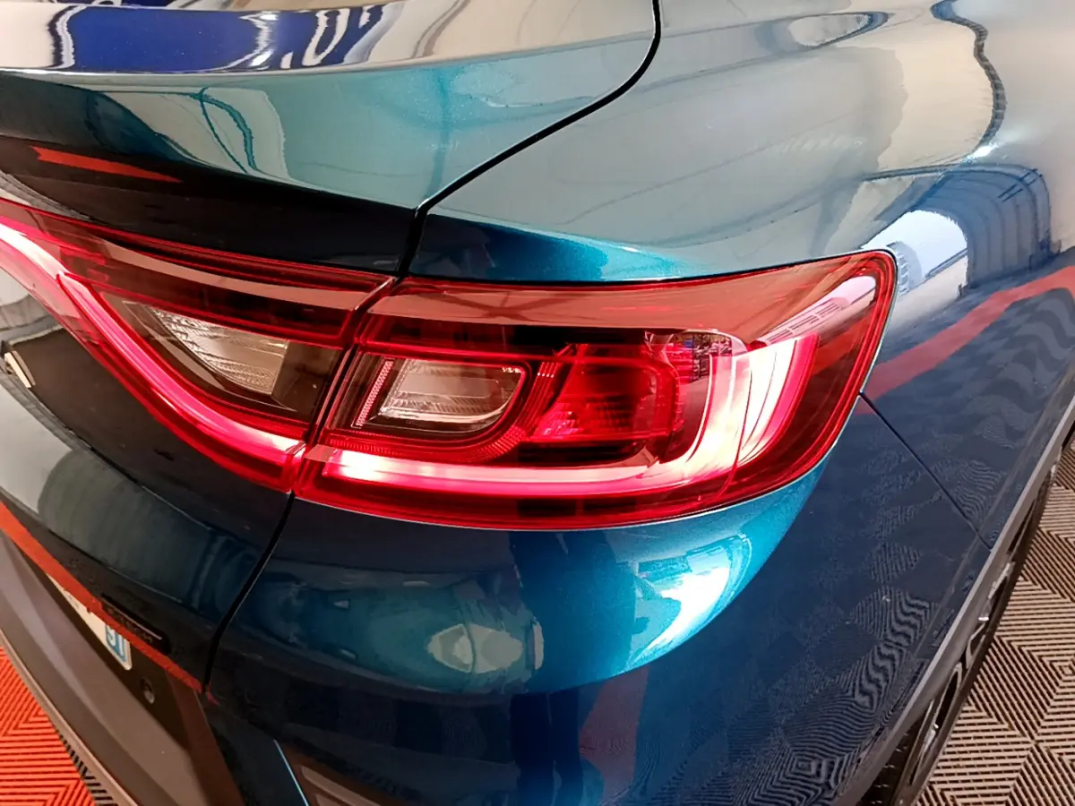 Gros plan sur le feu arrière droit rouge d’un Renault Arkana bleu métallisé 2023, avec reflet sur la carrosserie.