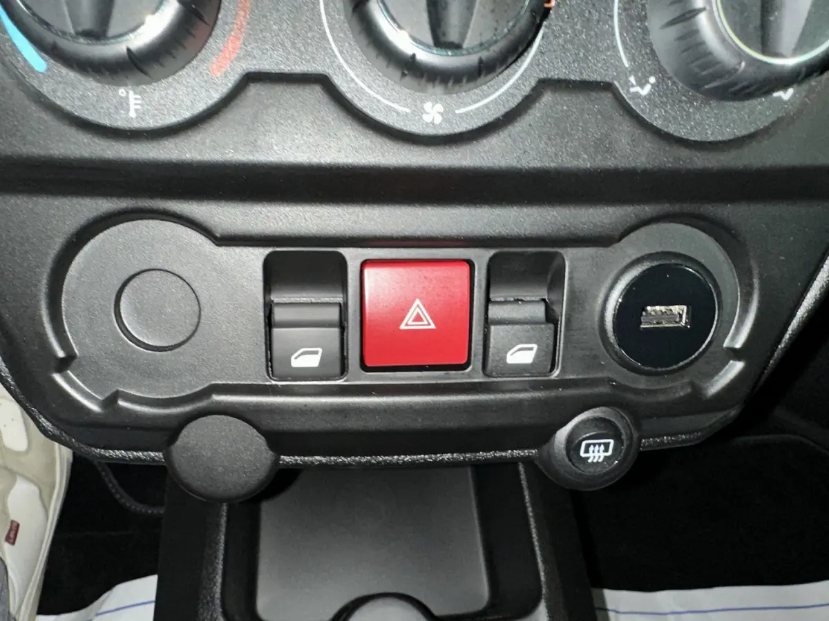 Gros plan sur la console centrale noire de l'AIXAM AMBITION rouge 2025, avec boutons de vitres et alerte au centre.