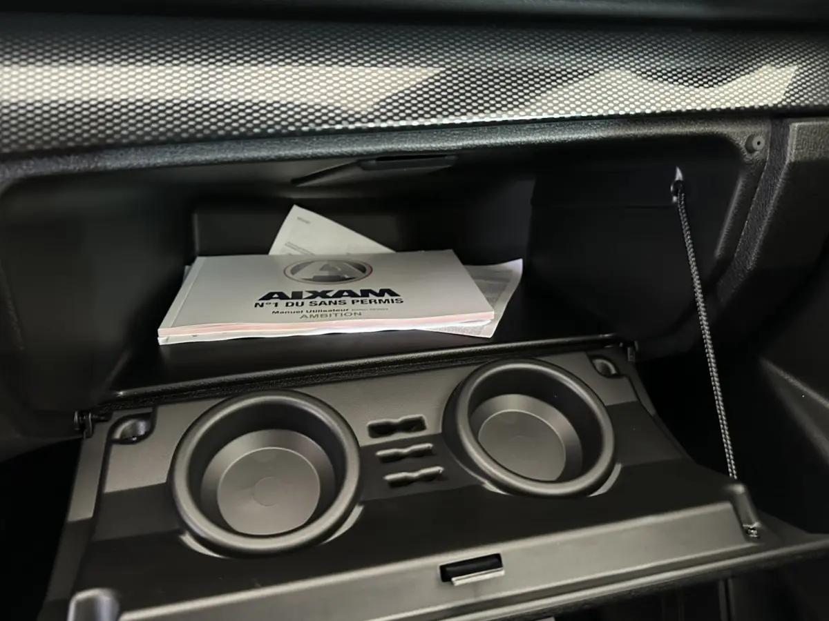 Gant de boîte à gants ouvert avec manuel utilisateur Aixam Ambition visible, intérieur noir sobre et fonctionnel.