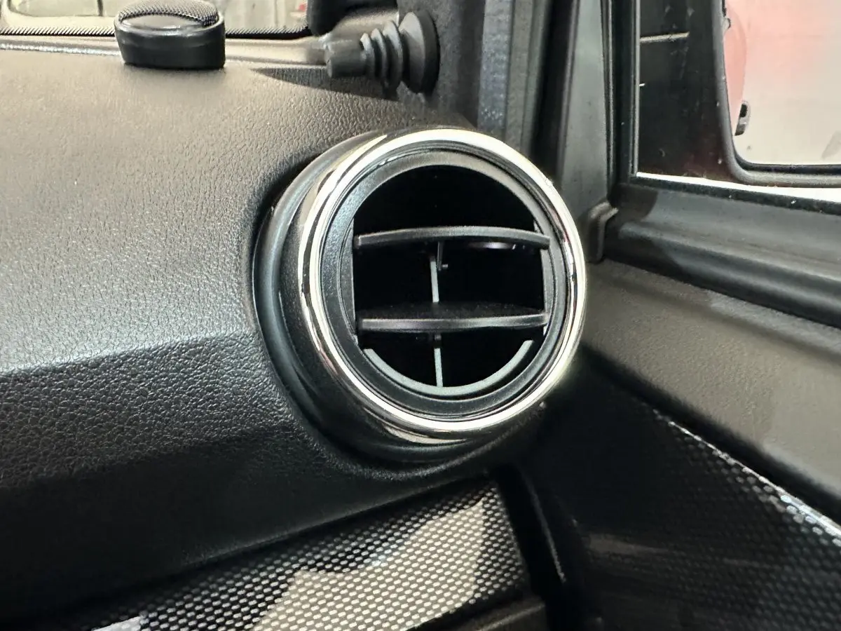 Détail de la sortie d'air ronde chromée côté conducteur dans l'habitacle d'une Aixam Ambition rouge 2025.