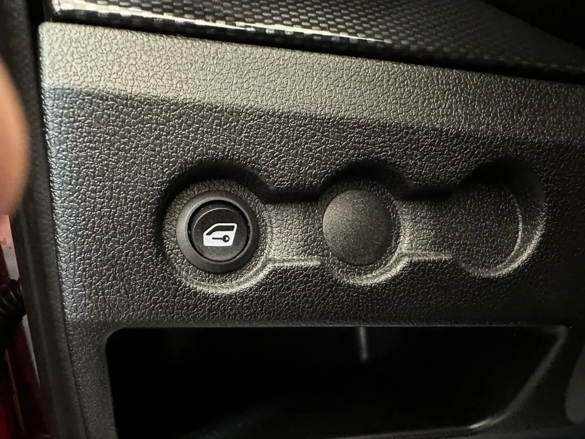 Bouton d'ouverture du coffre sur tableau de bord noir texturé d'une Aixam Ambition rouge 2025.