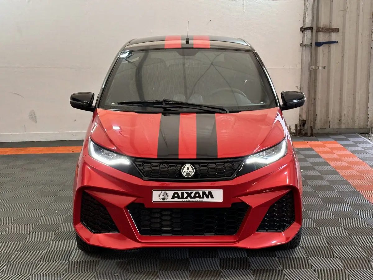 Vue frontale d'une Aixam Ambition 0.5 City Coupe GTI rouge avec bandes noires et rétroviseurs noirs dans un garage.