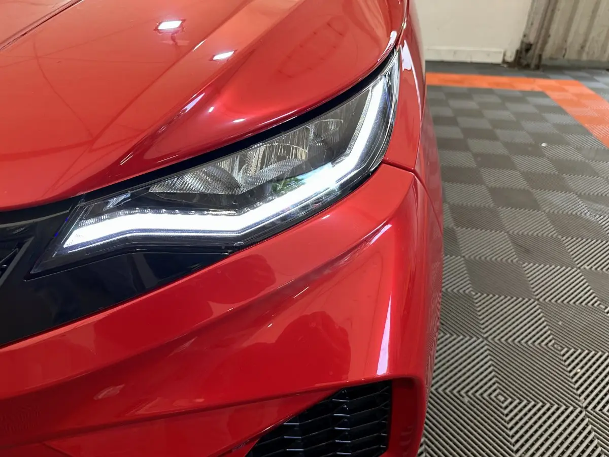 Gros plan sur le phare avant droit allumé d'une AIXAM AMBITION rouge 2025, soulignant ses lignes modernes.