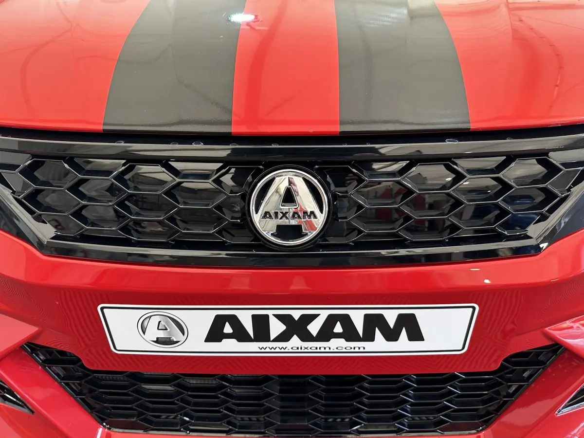 Gros plan sur la calandre noire et le logo AIXAM d'une AMBITION rouge avec bandes noires sur le capot.
