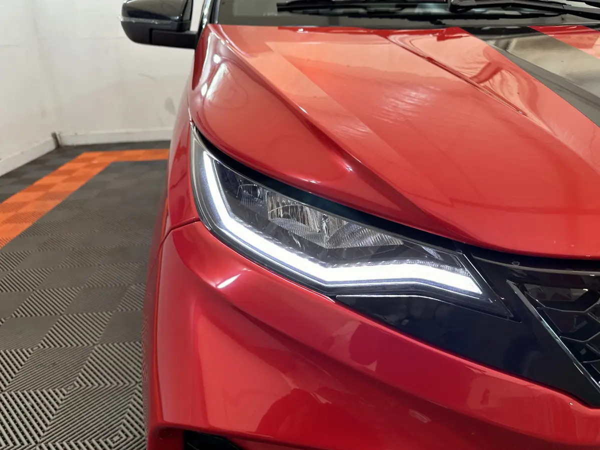 Gros plan sur le phare avant gauche allumé d'une Aixam Ambition rouge 2025 avec rétroviseur caméra visible.