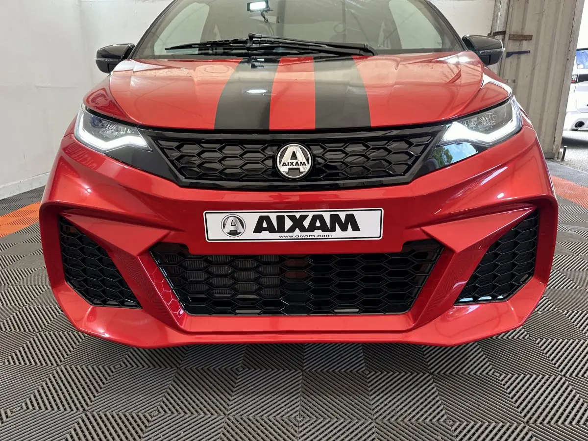 Vue frontale rapprochée de l'AIXAM AMBITION rouge 2025 avec bandes noires et calandre hexagonale marquée.
