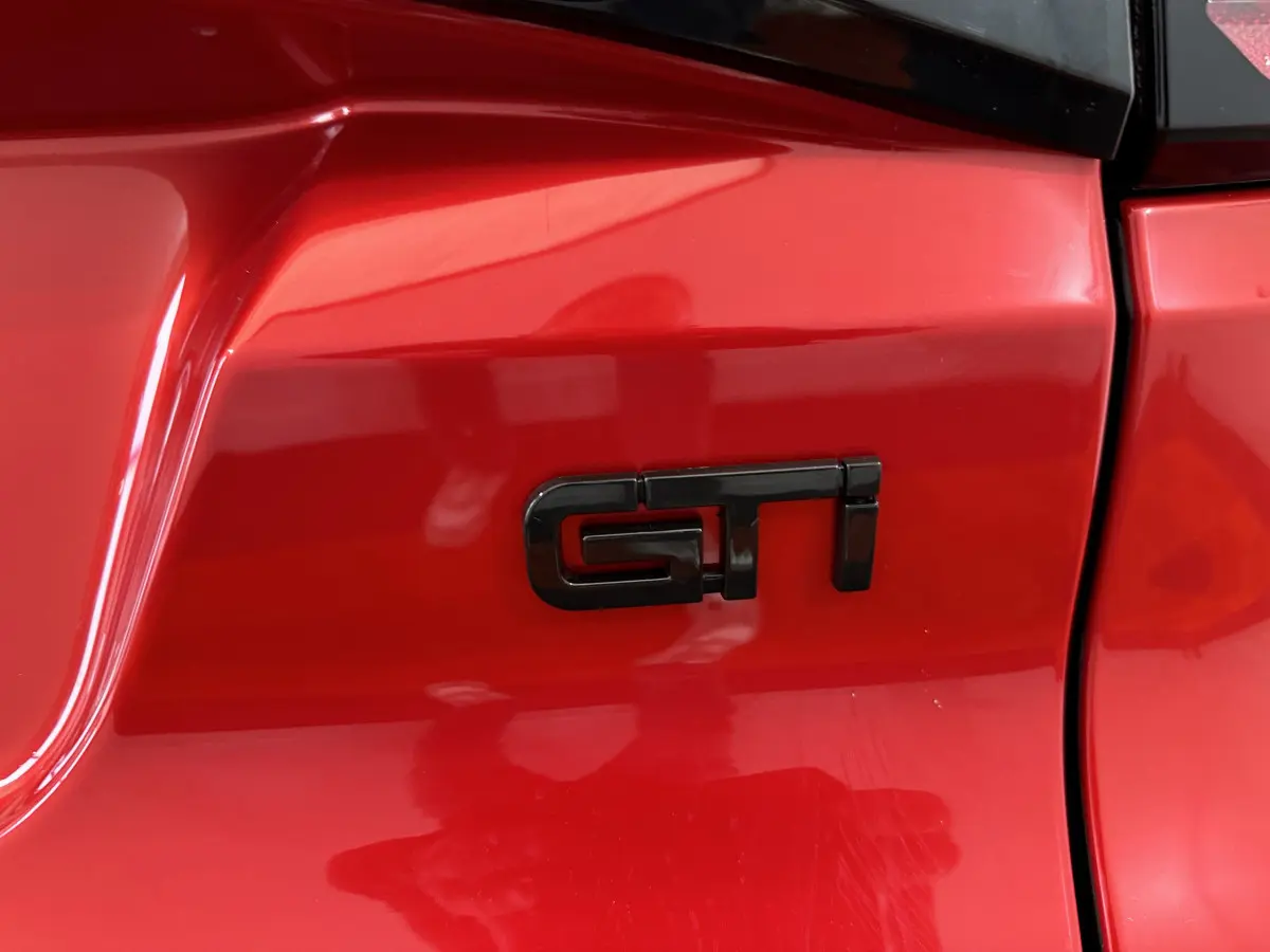 Gros plan sur l’inscription GTI noire sur la carrosserie rouge vif de l’AIXAM AMBITION 0.5 CITY COUPE GTI E5+ côté conducteur.