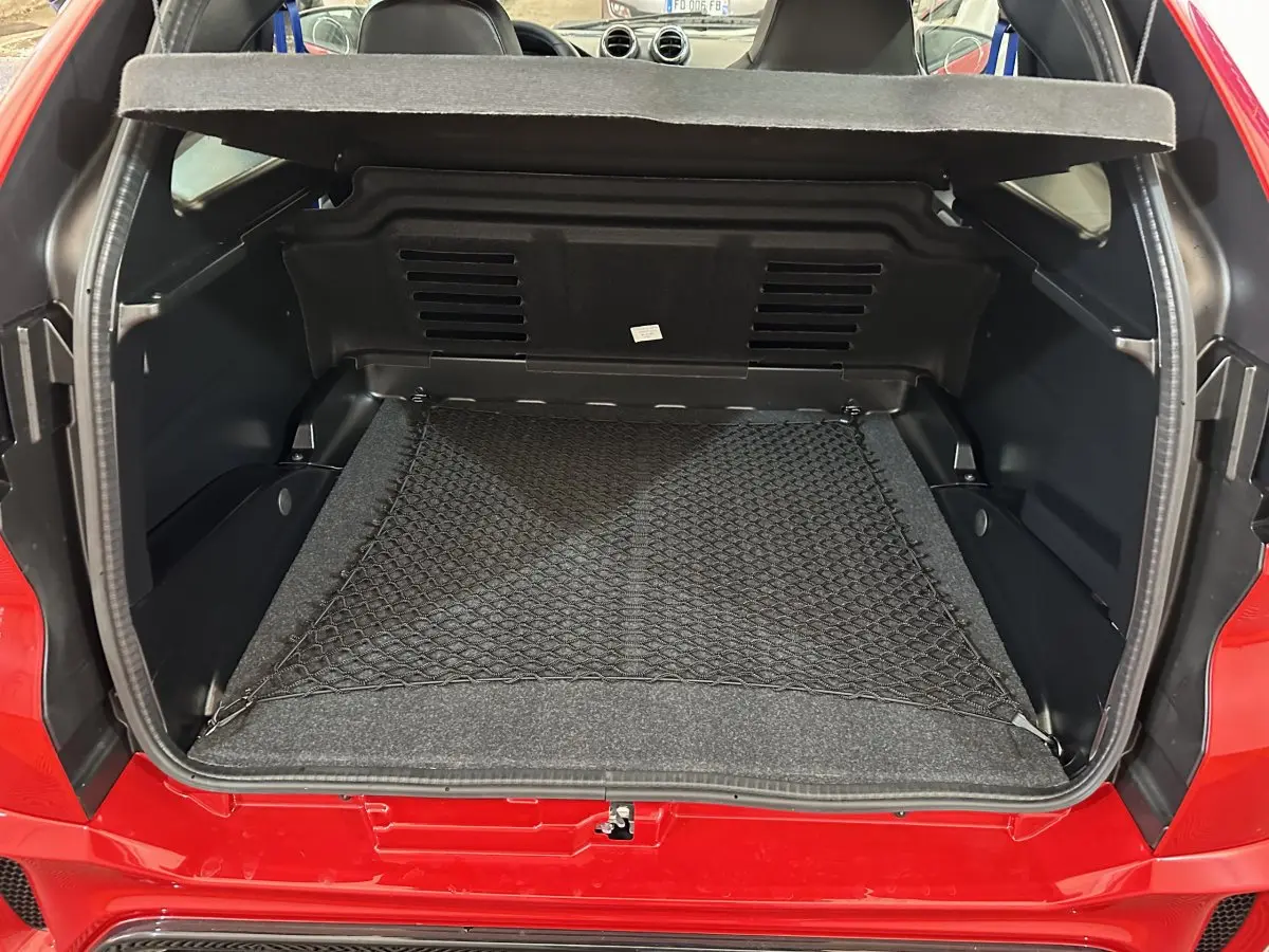 Coffre ouvert vu de l'arrière d'une Aixam Ambition rouge 2025 avec filet de rangement et intérieur noir.