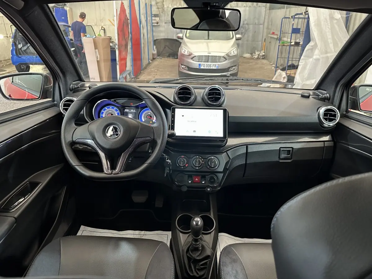 Vue intérieure de l'AIXAM AMBITION 0.5 CITY COUPE GTI E5+ 2025, tableau de bord et volant noir avec écran tactile central.
