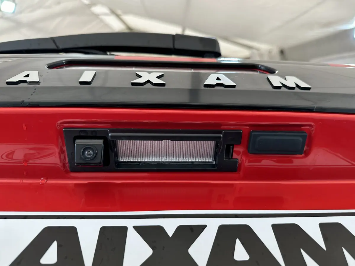 Gros plan sur la caméra de recul intégrée au hayon rouge de l'AIXAM AMBITION 2025, avec logo visible.
