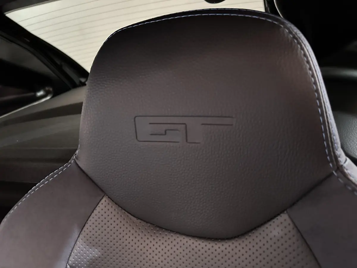 Gros plan sur l'appui-tête en cuir noir embossé du logo GT dans l'habitacle de l'AIXAM Ambition rouge.