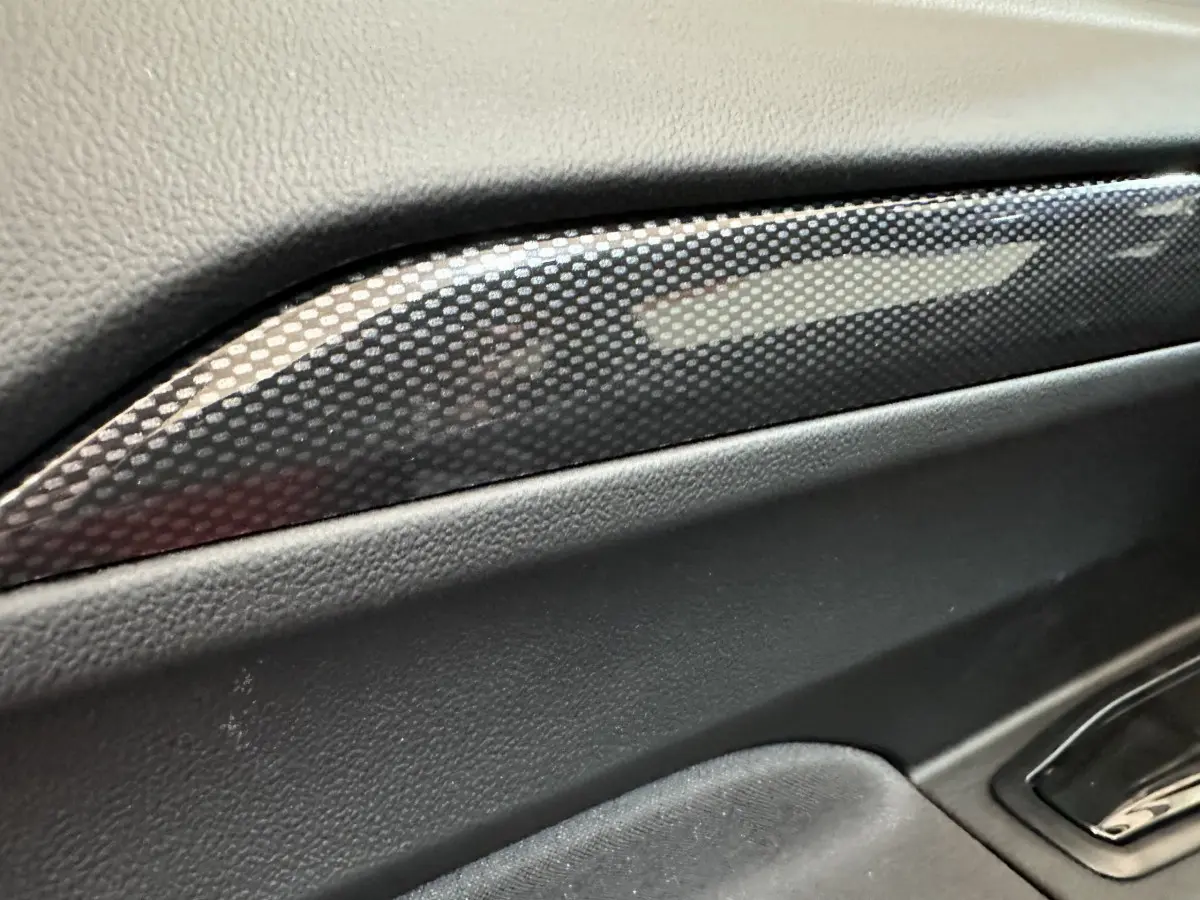 Gros plan sur la garniture intérieure noire avec insert effet carbone de l'AIXAM AMBITION rouge, côté conducteur.