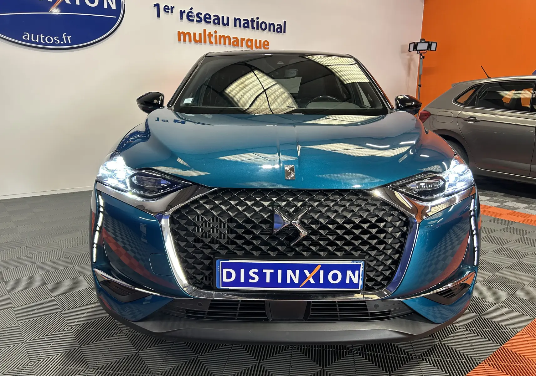 Vue frontale d'un DS3 Crossback Bleu Millenium avec calandre distinctive et phares LED allumés en intérieur showroom.