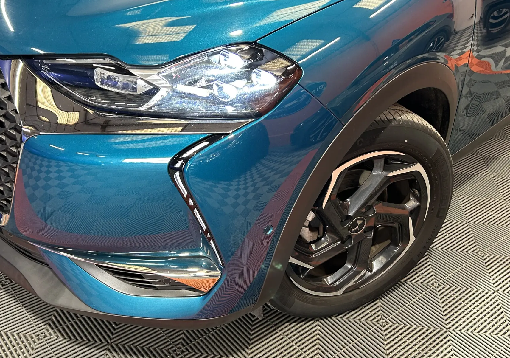 Gros plan sur l'avant droit bleu Millenium du DS3 Crossback avec phare allumé et jante noire à détails argentés.