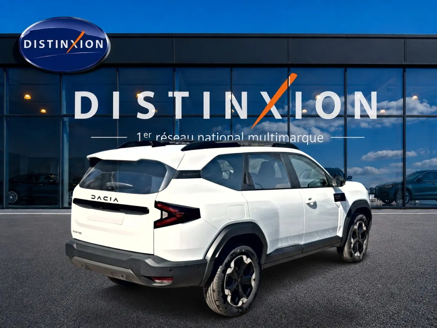 Vue 3/4 arrière droite du Dacia Bigster blanc avec barres de toit noires et jantes alliage distinctives.