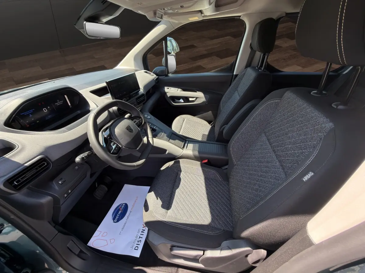 Vue intérieure côté conducteur du Peugeot Rifter 2026, sièges tissu gris et tableau de bord moderne avec écran tactile.
