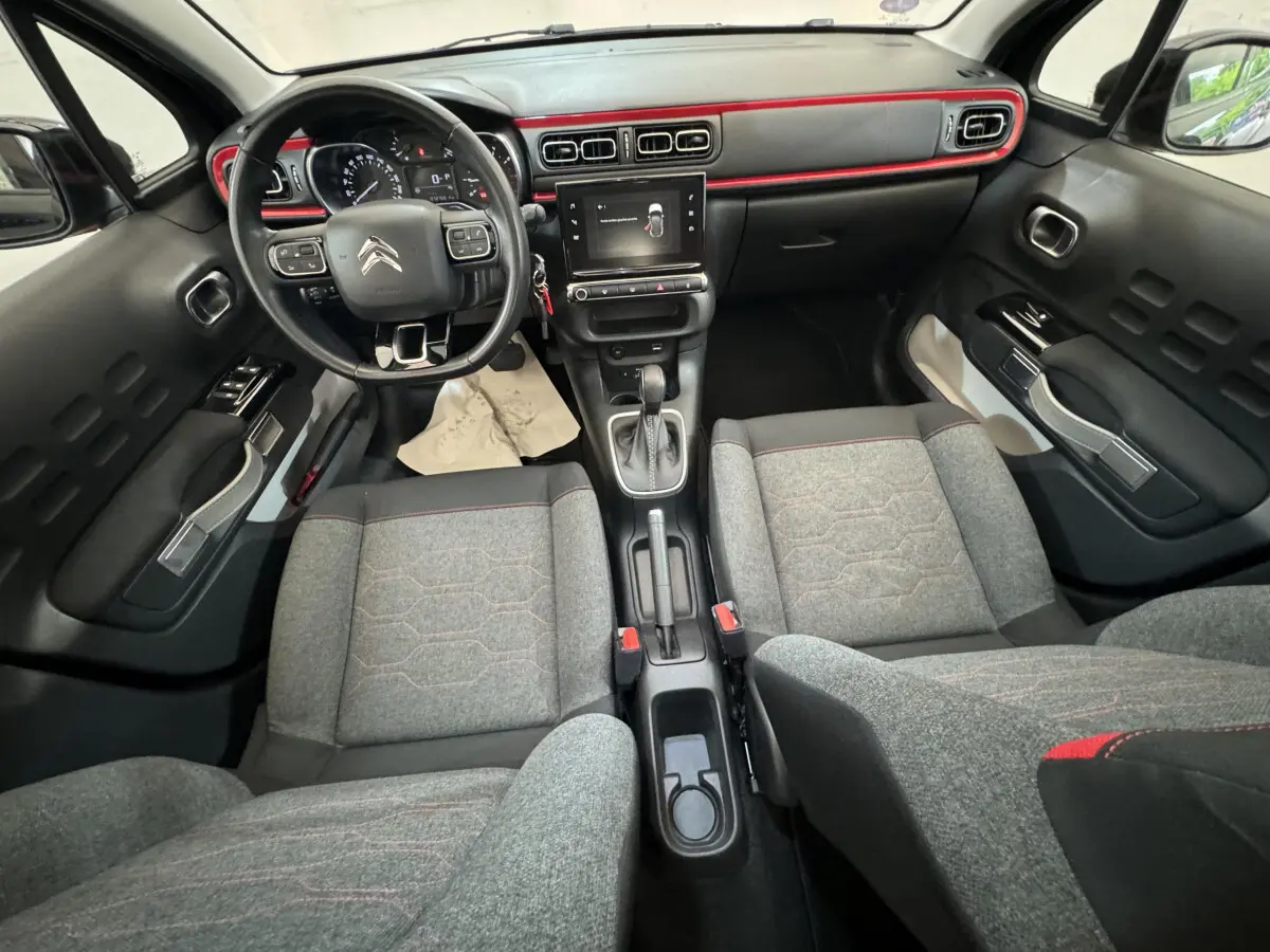 Vue intérieure avant de la Citroën C3 2019, tableau de bord noir avec touches rouges et sièges gris à surpiqûres rouges.