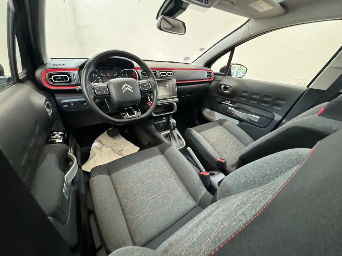 Vue intérieure avant droite de la Citroën C3 noire 2019 avec tableau de bord noir et touches rouges décoratives.