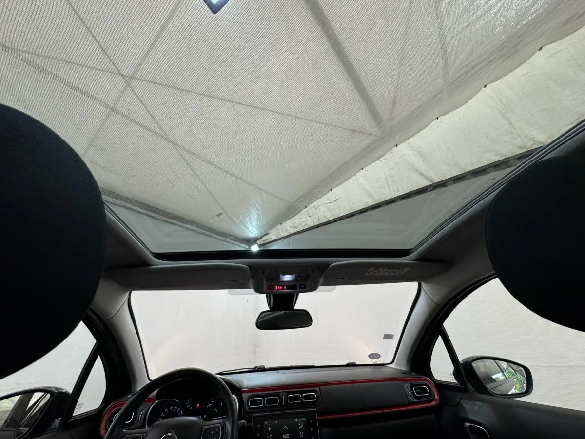 Vue intérieure avant de la Citroën C3 noire 2019, avec toit panoramique et tableau de bord à liseré rouge.