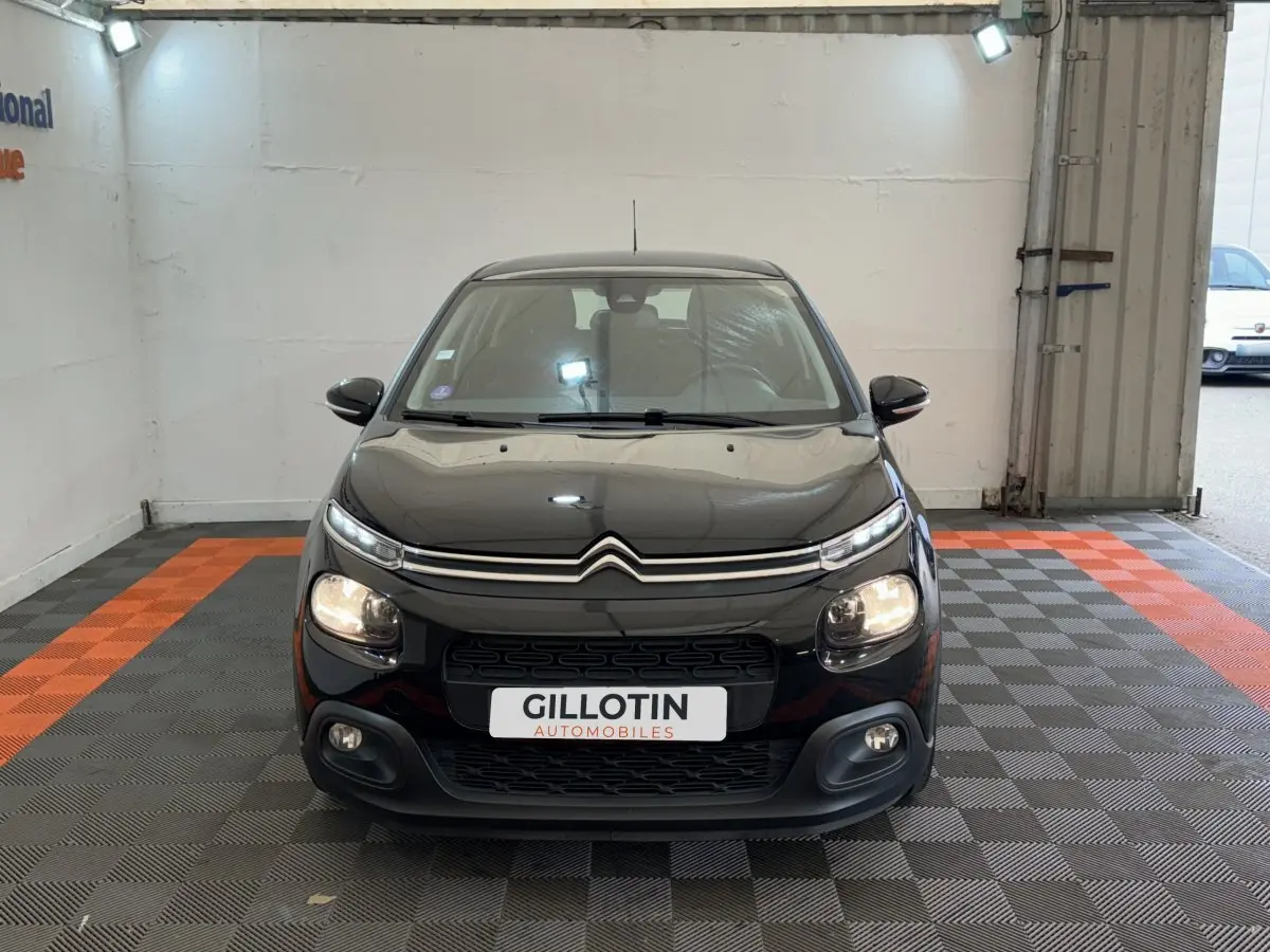 Citroën C3 noire vue de face dans un showroom, avec phares allumés et calandre distinctive.