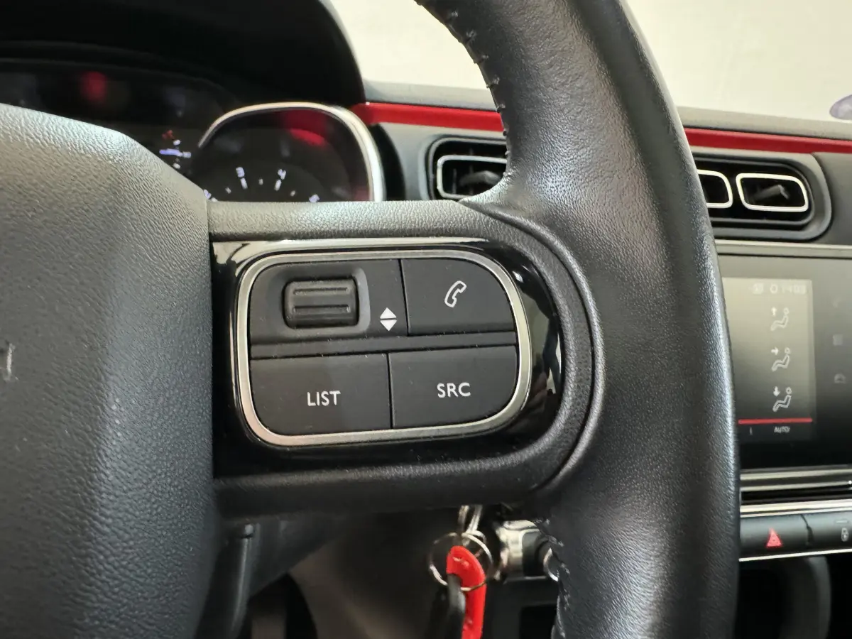 Gros plan sur les commandes gauche du volant cuir noir d'une Citroën C3 noire, avec tableau de bord et écran tactile visibles.