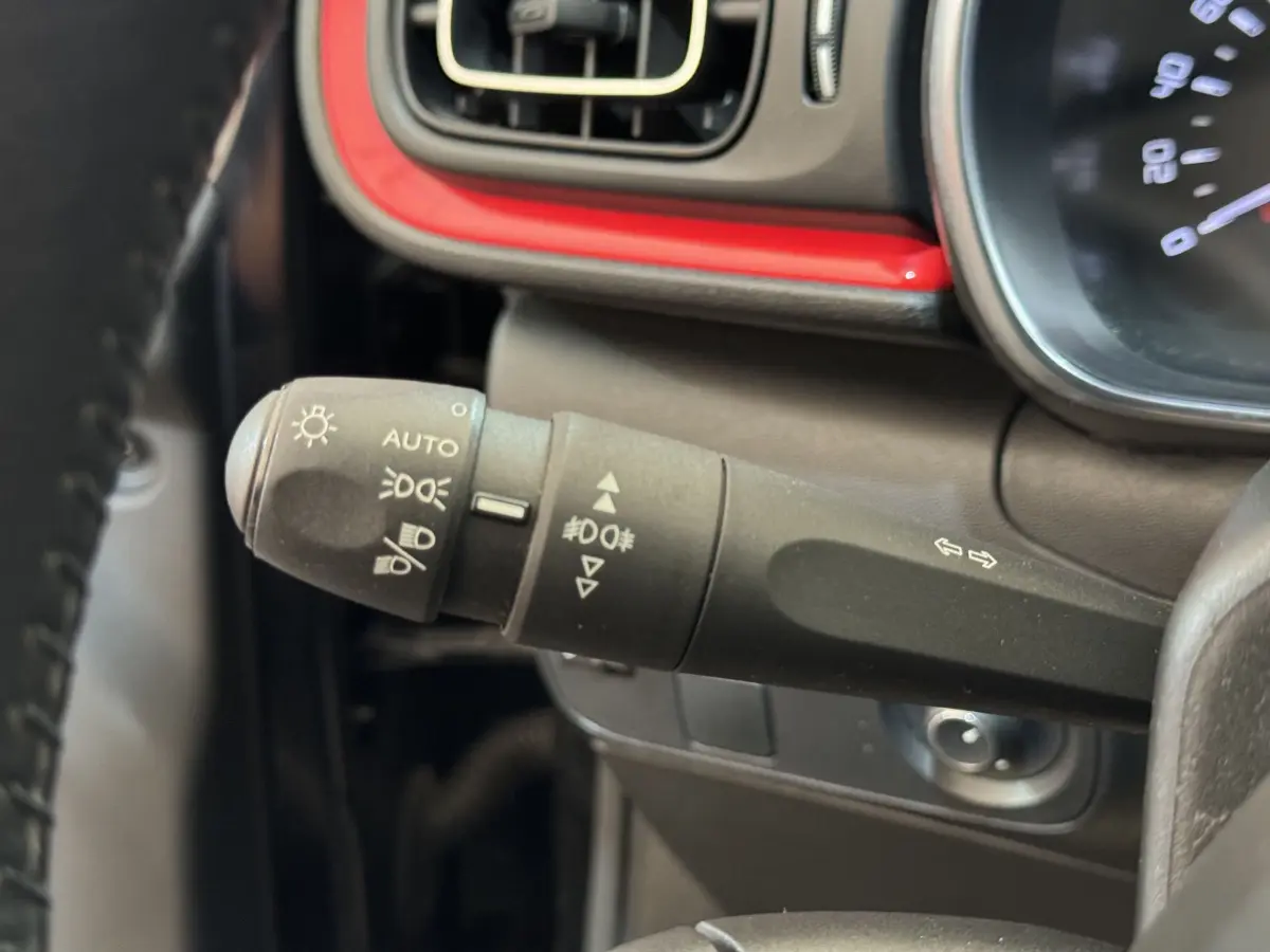 Gros plan sur la commande des phares et clignotants à gauche du volant dans l’habitacle noir et rouge de la Citroën C3 2019.