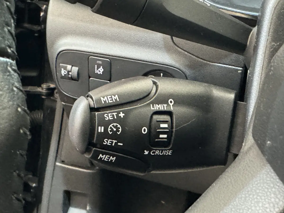 Gros plan sur la commande de régulateur de vitesse noire à gauche du volant d'une Citroën C3 noire de 2019.