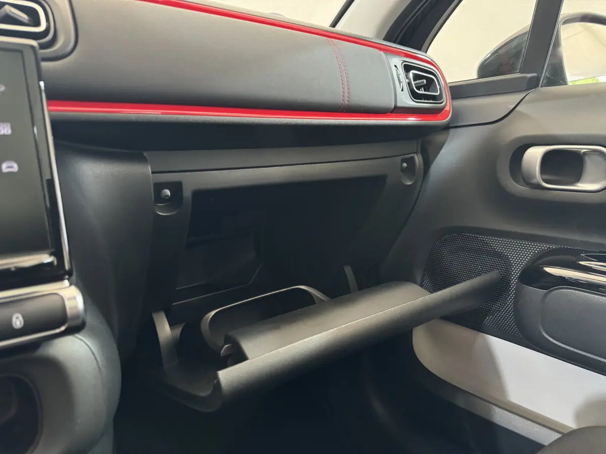 Intérieur côté passager de la Citroën C3 2019 noir, avec boîte à gants ouverte et bandeau rouge décoratif sur le tableau de bord.