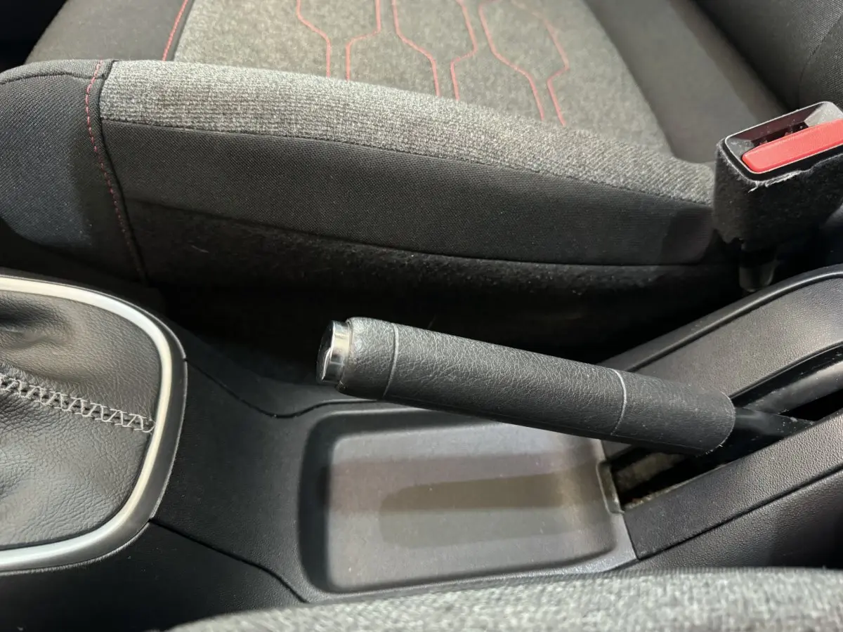 Gros plan sur frein à main en cuir noir et siège tissu gris avec surpiqûres rouges dans Citroën C3 noire 2019.