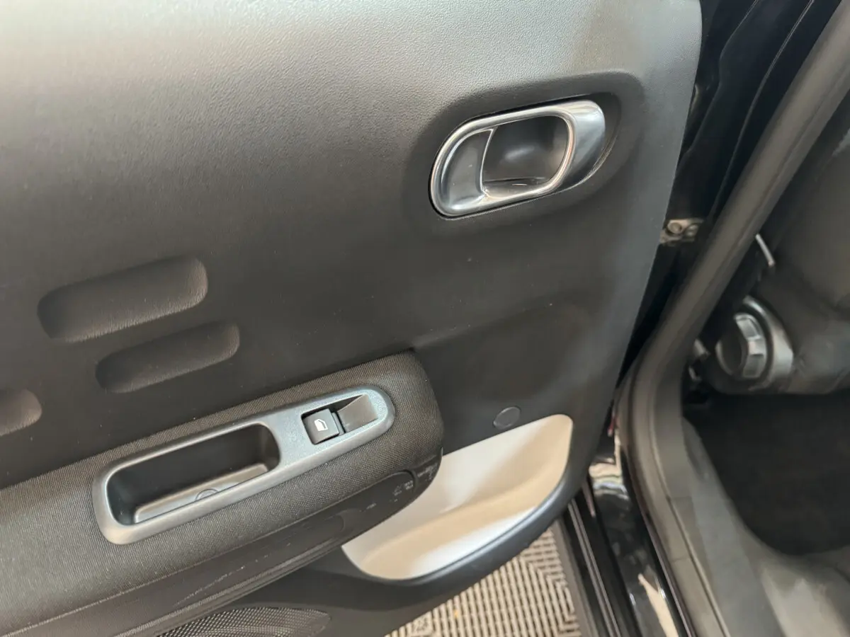 Poignée intérieure et commande de lève-vitre sur la porte arrière droite noire d'une Citroën C3 2019 Shine Business.