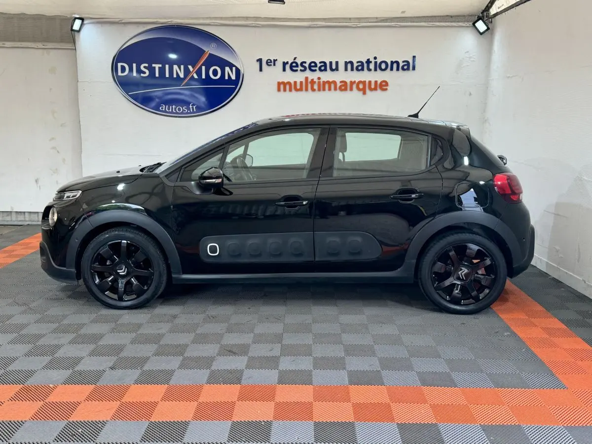 Profil côté gauche d'une Citroën C3 noire 2019 avec protections latérales caractéristiques et jantes noires en intérieur showroom.