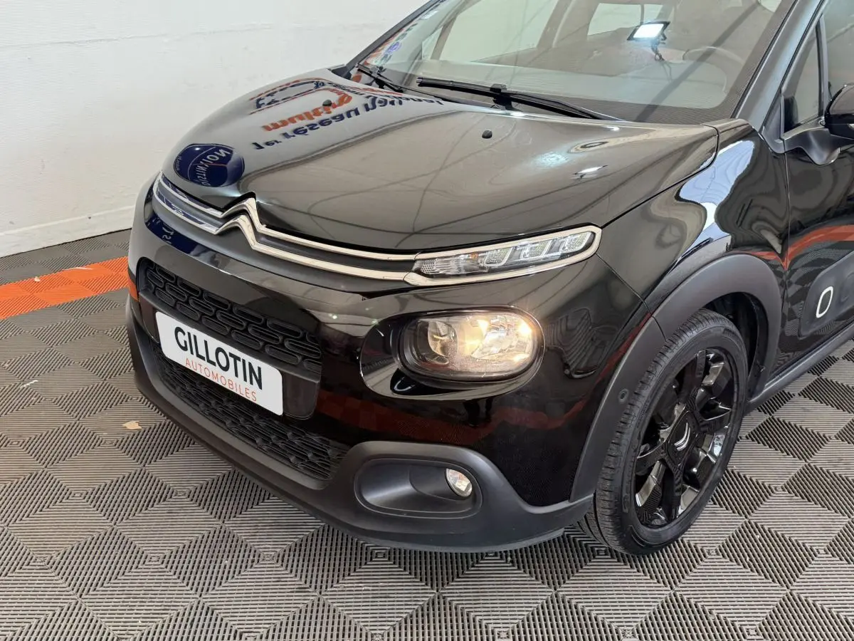 Vue 3/4 avant droite d'une Citroën C3 noire avec phares allumés et jantes noires brillantes.