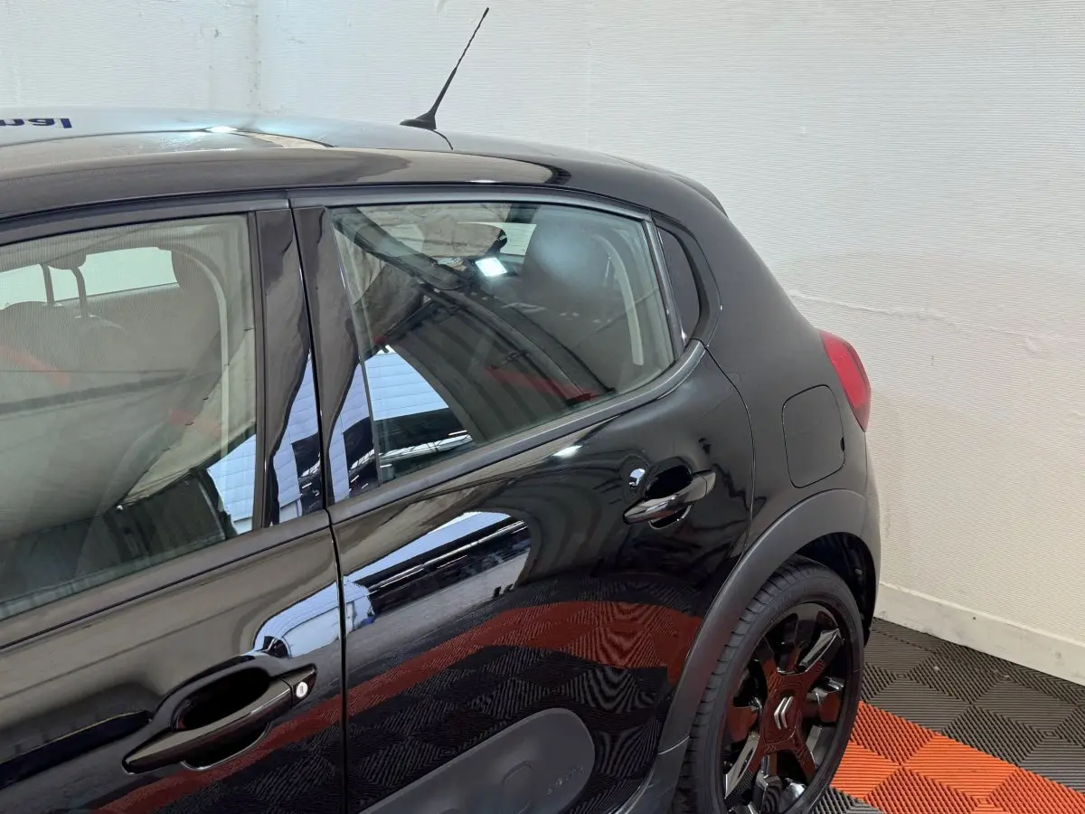 Vue latérale droite sur la partie arrière d'une Citroën C3 noire avec jantes noires et poignées de porte ton caisse.
