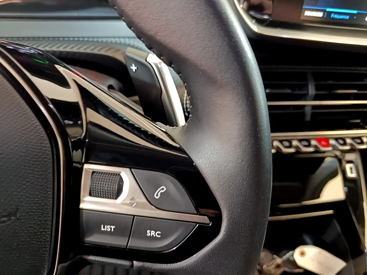 Gros plan sur le volant cuir noir de la Peugeot 2008 2022 avec commandes audio et palettes au volant.