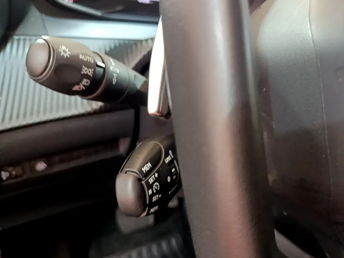 Gros plan sur la commande de régulateur de vitesse et le commodo d’éclairage, intérieur noir du Peugeot 2008 gris foncé.