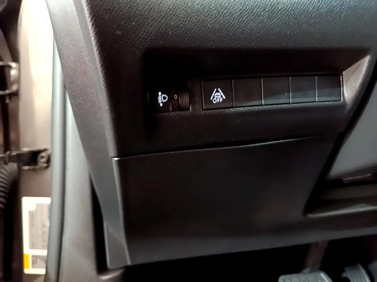 Gros plan sur les commandes de réglage des phares et d'alerte de franchissement de ligne à gauche du volant du Peugeot 2008 gris foncé.