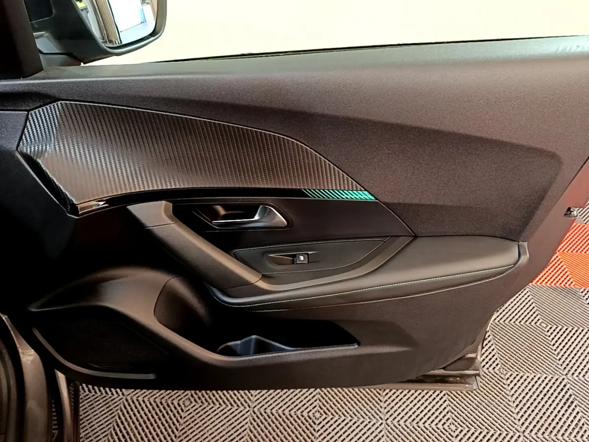 Vue rapprochée de la porte côté gauche du Peugeot 2008 gris foncé avec insert décoratif noir brillant et bouton de vitre électrique.